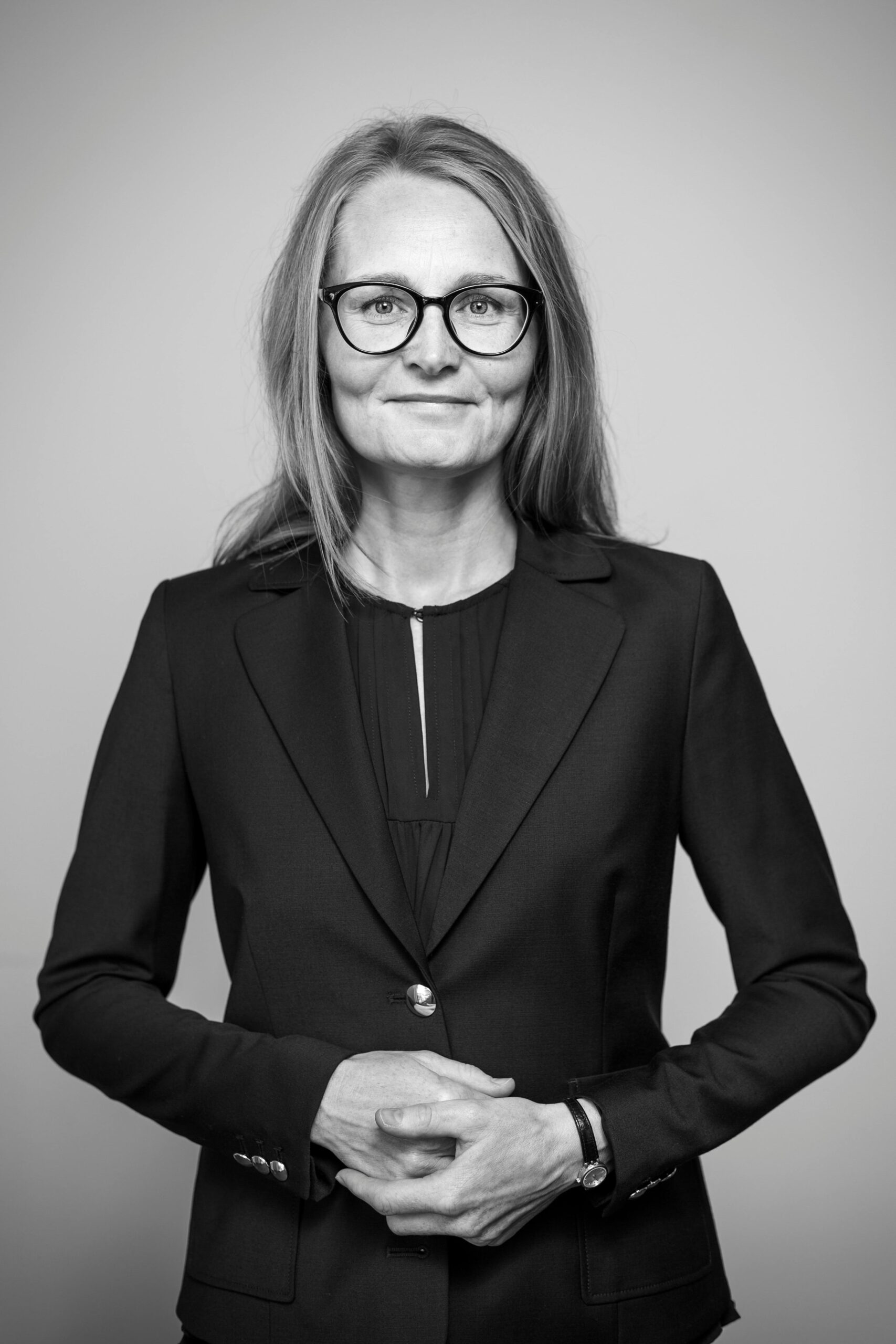 Black and white portrait of a confident businesswoman wearing glasses, posing with a smile.